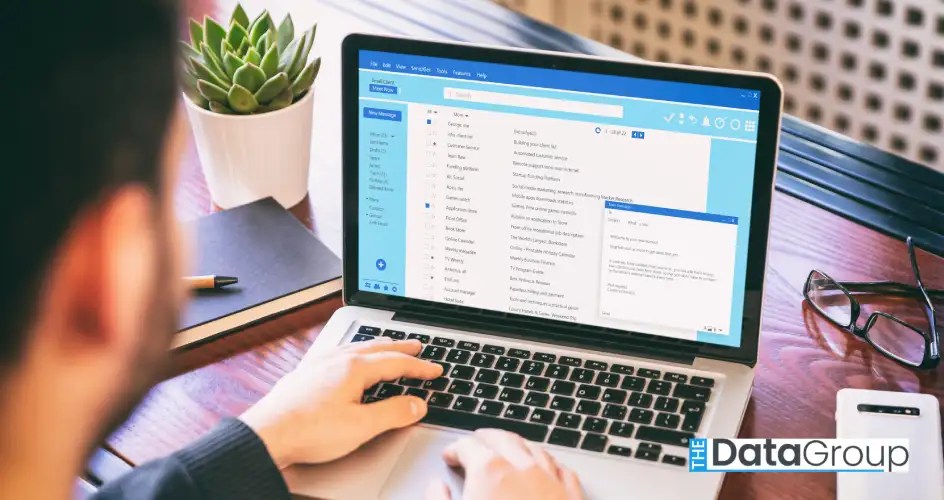 A workspace scene shows a person in a dark jacket working at a light-colored laptop, with email open on the screen, accompanied by a pen, notebook, succulent, and glasses. The composition is ideal for illustrating themes of business, technology, and working from home. The layout is ideal for conveying a sense of modern professionalism, suitable for corporate communications, tech blogs, or marketing materials promoting remote work solutions.
