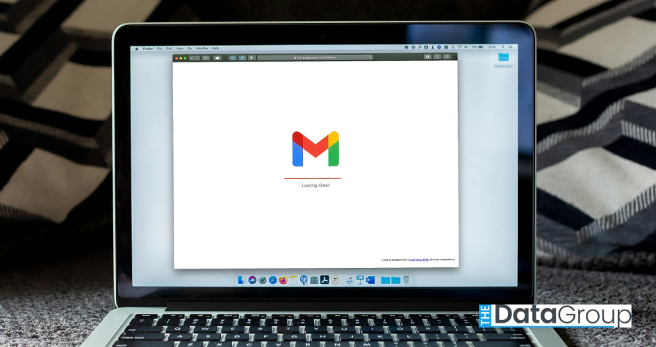 Open laptop sitting on a carpet with the Gmail loading screen centered on the display. The screen shows the Google Gmail logo and the text "Loading Gmail"