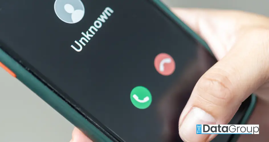 An extreme close-up shows a mobile phone held in a hand with an unknown caller displayed on the screen. A green phone icon is also displayed, as is a red icon. The mood is tense. This photo could be used for projects centered around scam phone calls, technology, social issues, and modern life.