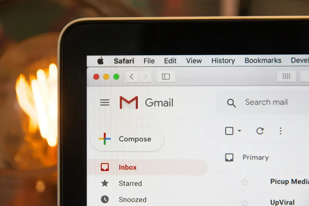 Close-up of a laptop screen displaying the Gmail interface in a Safari browser, showing the sidebar with options like Compose, Inbox, and Starred, with a blurred background.